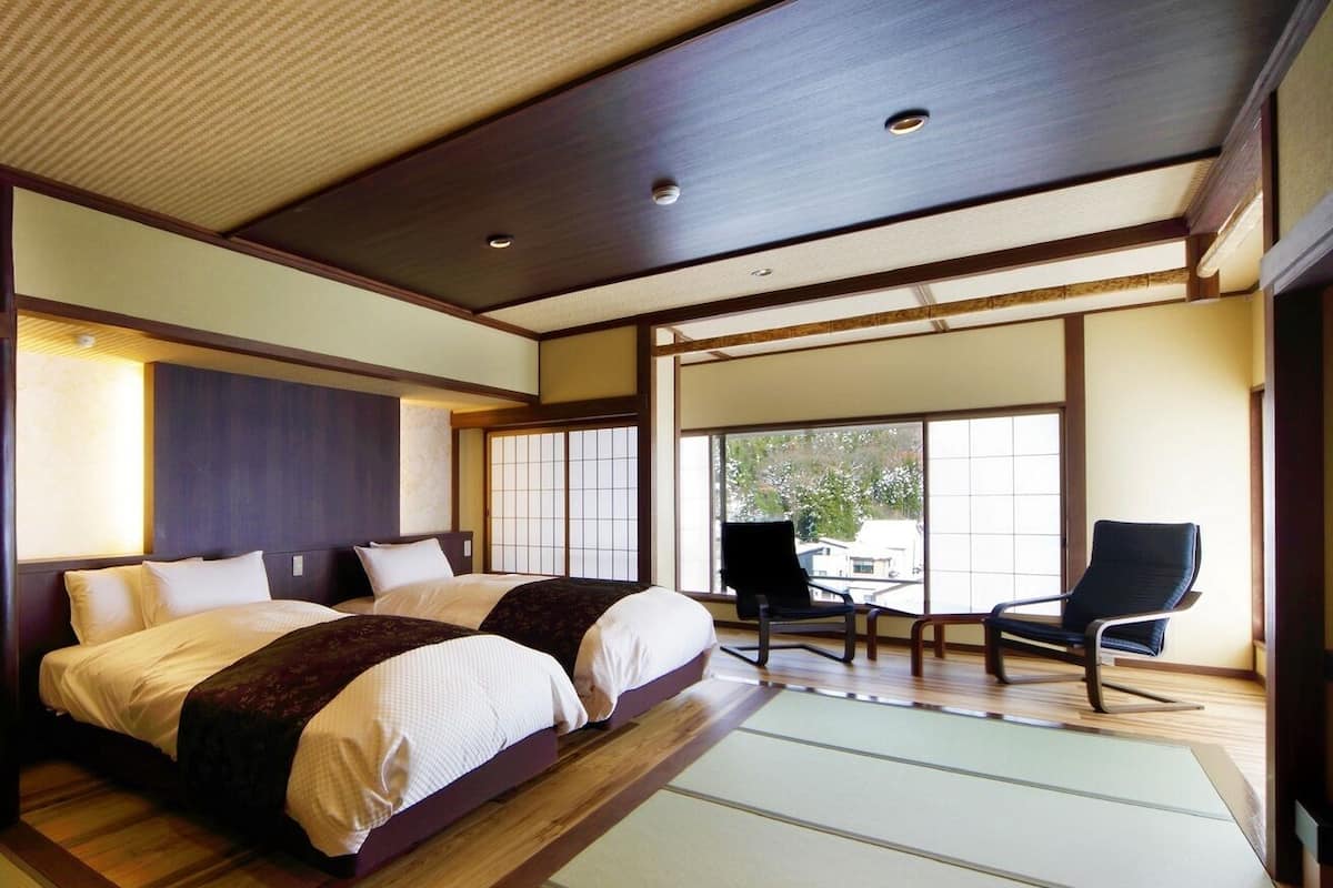 A traditional Japanese-style bedroom with tatami flooring, a large bed, sliding doors, and a view of the outside.