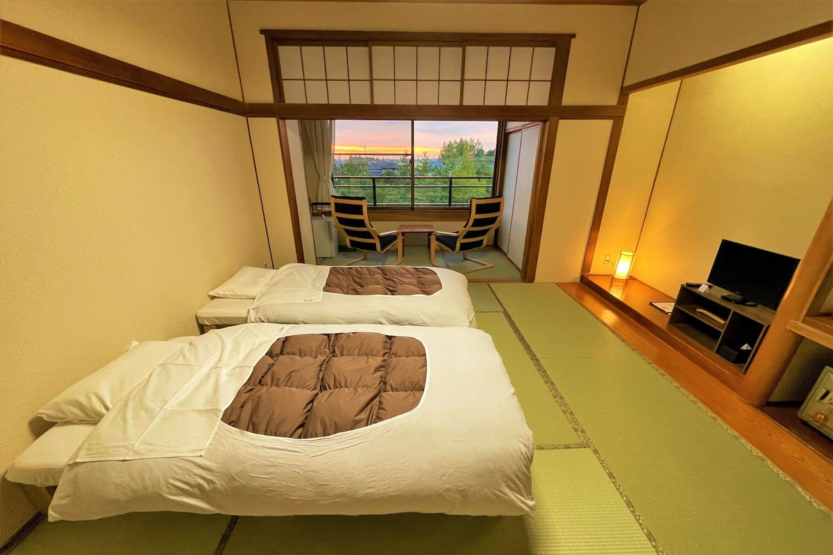 A hotel room with two beds, a TV, and a view of the outdoors.