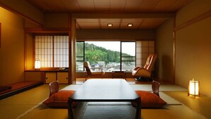 A tatami mat room with a low table, cushions, and a view of a forest through large windows. - Hotel Hisagoso (Shibata)