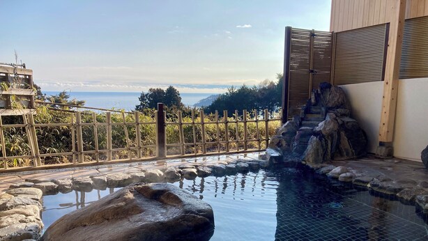 Un área de piscina tranquila al aire libre con vista despejada al mar, rodeada de formaciones rocosas naturales y vallas de bambú.