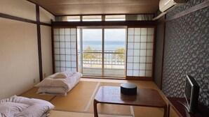 Una habitación con suelo de tatami, un futón, una mesita, un televisor y vista al mar.