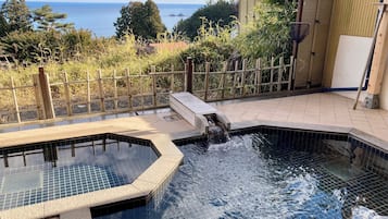A swimming pool with a waterfall feature, surrounded by a bamboo fence and a view of the sea.