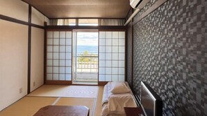 Una habitación japonesa tradicional con suelo de tatami, puertas correderas shoji, una cama con ropa blanca y vistas al mar.