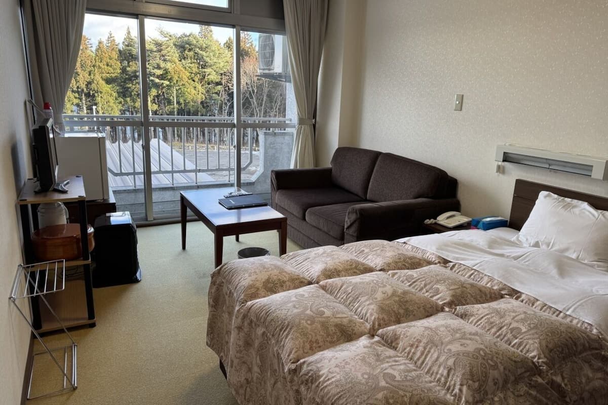 Una habitación de hotel con una cama, un sofá, una mesita, un escritorio y una ventana con cortinas.