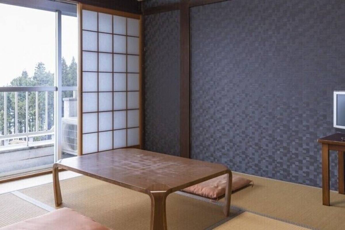 A traditional Japanese room with tatami flooring, a low table, a television on a wooden stand, and a sliding shoji screen.
