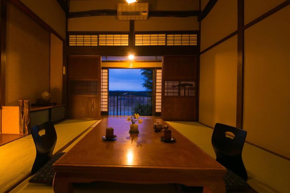Una tradizionale stanza giapponese con pavimenti in tatami, un tavolino e porte scorrevoli che danno su un balcone.
