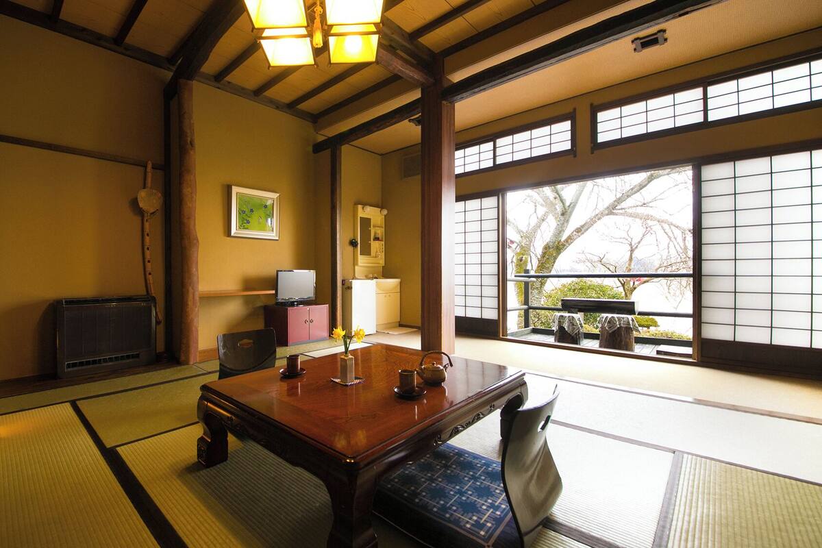 Una tradizionale stanza giapponese con pavimento in tatami, un tavolo di legno, un televisore e una finestra con paraventi shoji.