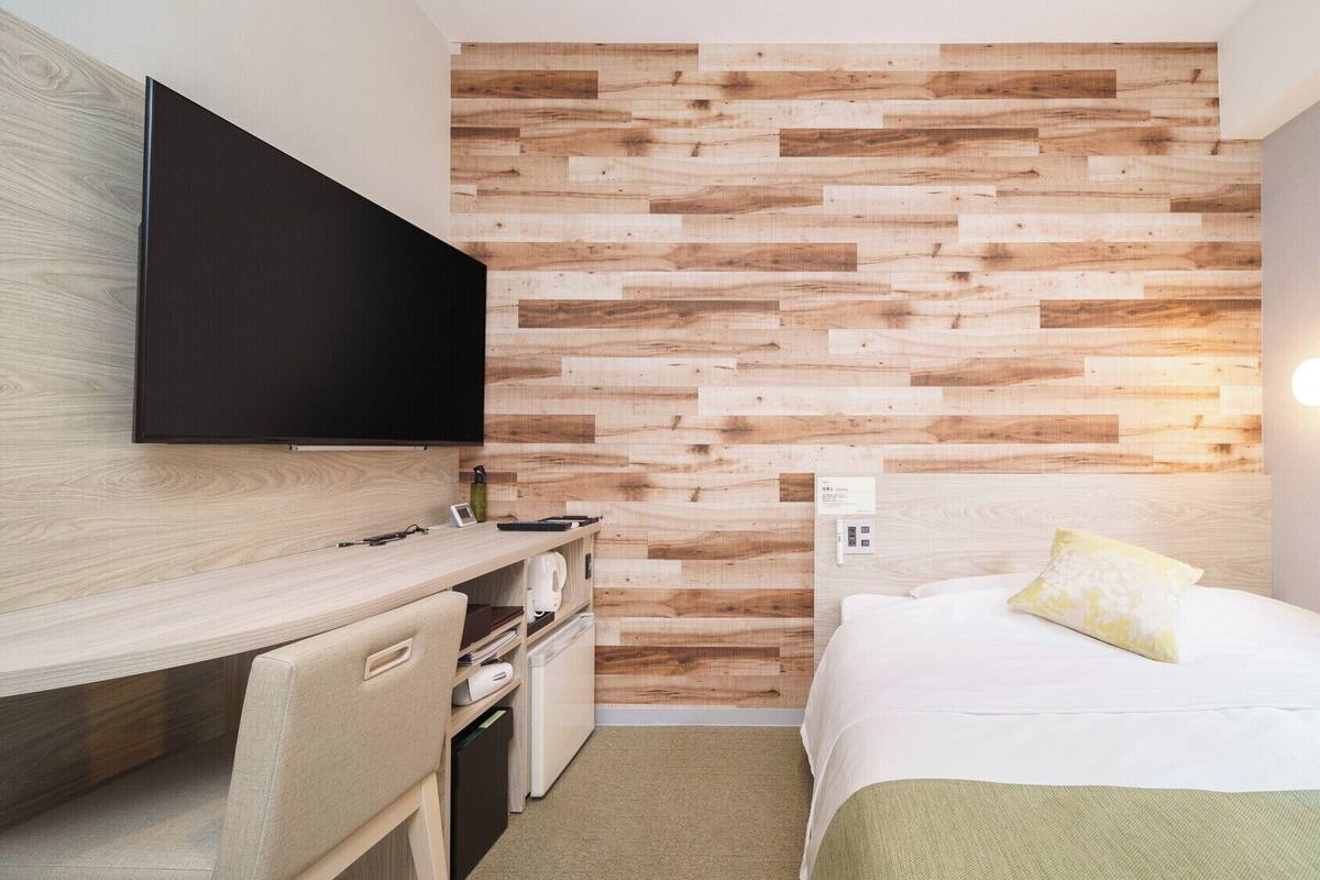 Camera d'albergo con pannello in legno, televisore a schermo piatto, scrivania con sedia, letto con cuscino e comodino.