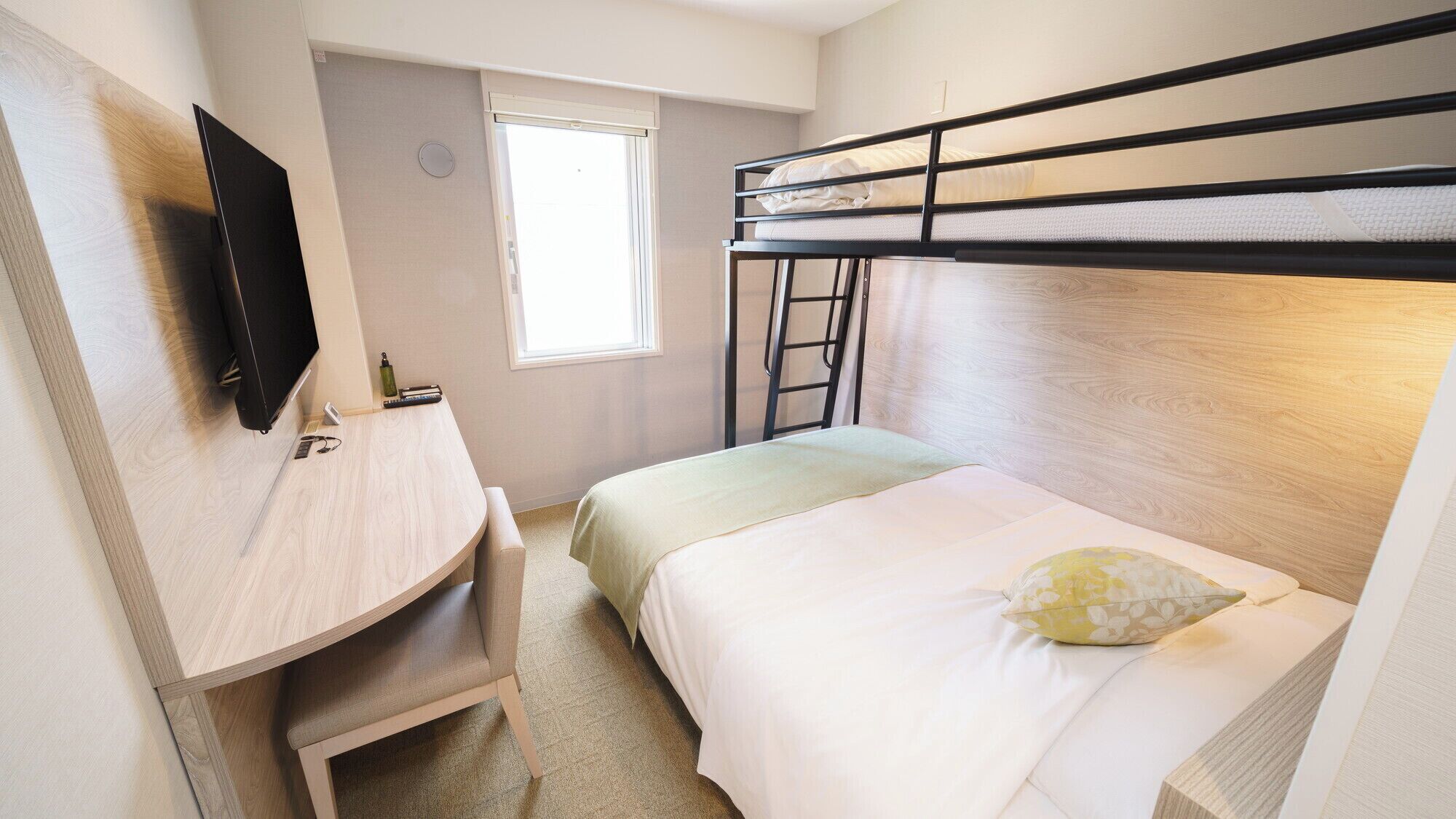 A bunk bed room with a TV mounted on the wall, a desk, and a window.