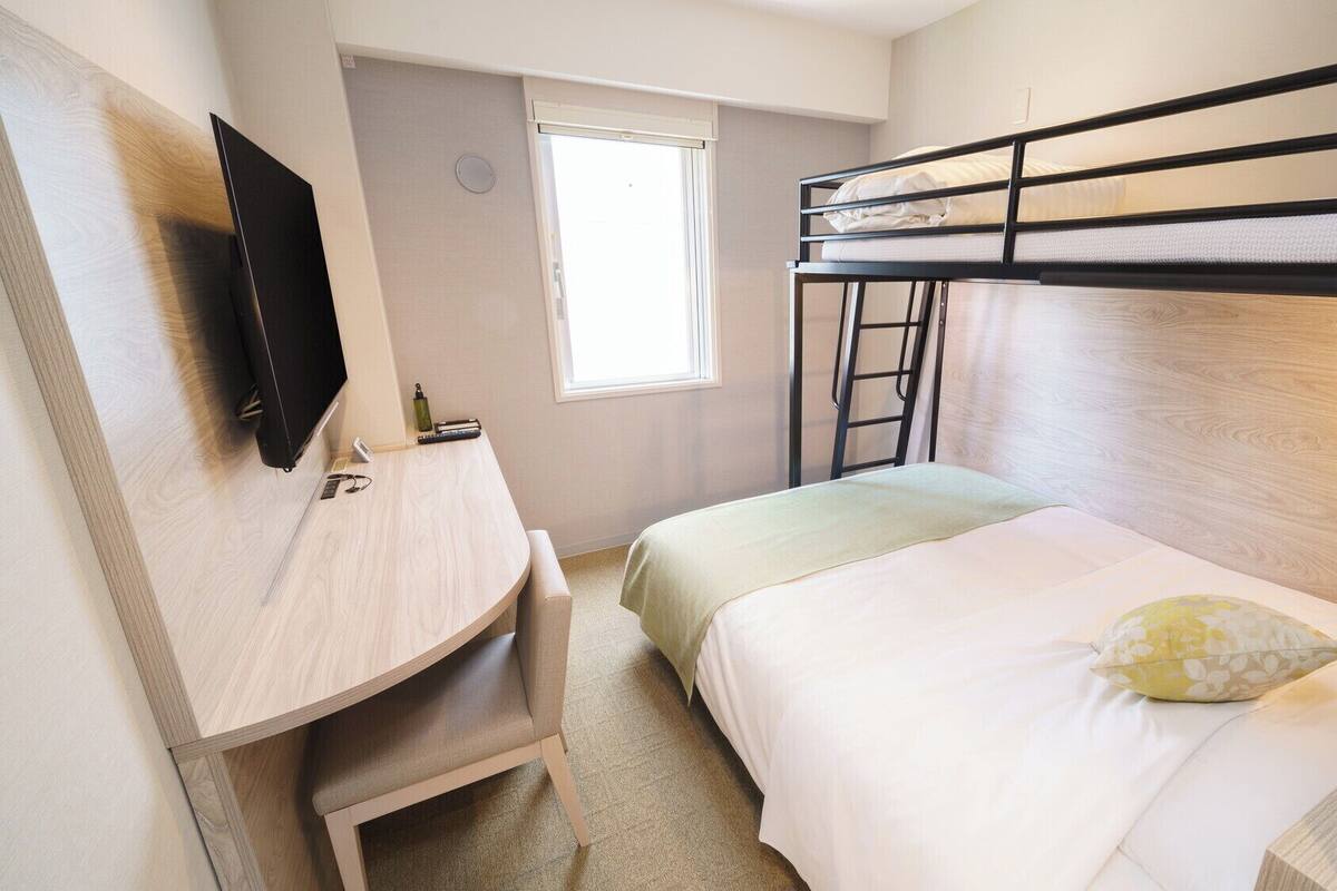 Camera con letto a castello, televisione a parete, una scrivania e una finestra.
