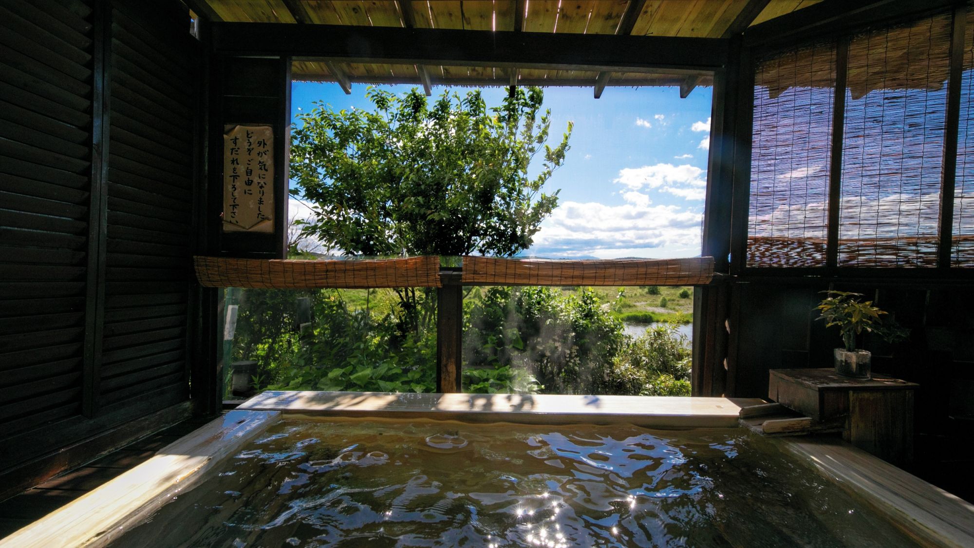 Perinteinen japanilainen onsen-kylpylä, jossa on puinen sisustus, näkymä vehreään maisemaan ja bambusta valmistettu sälekaihdin ikkunassa.