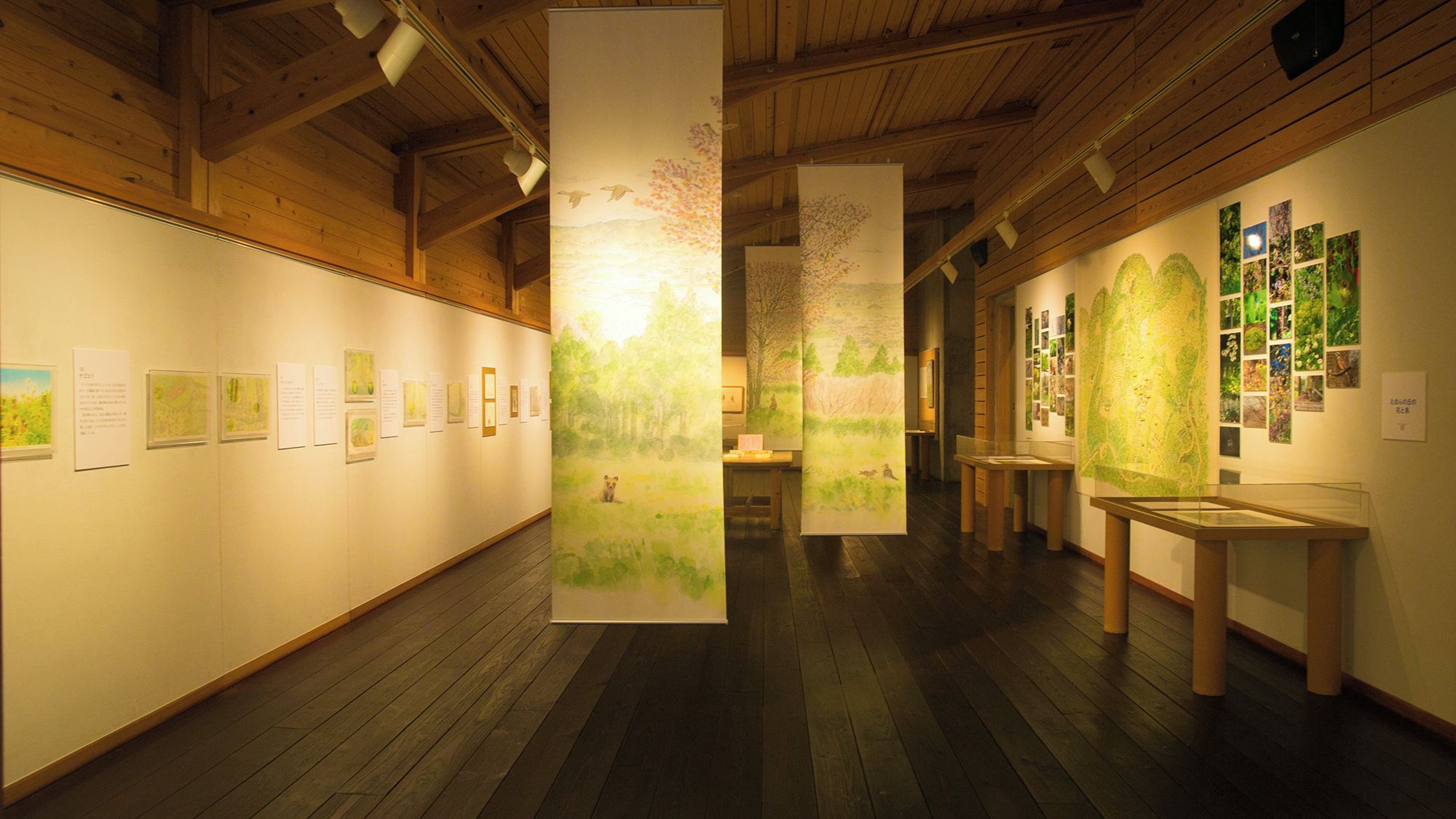 Eine Kunstgalerie mit Holzbalken an der Decke, Holzdielen und verschiedenen Kunstwerken an den Wänden.