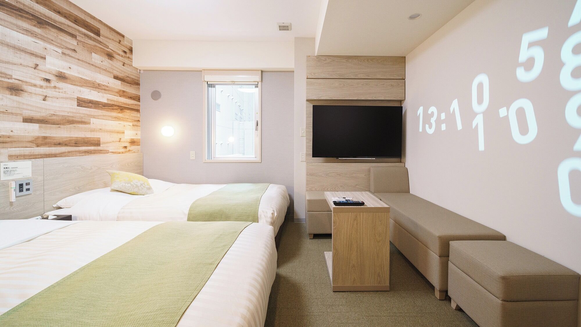 A modern hotel room with two beds, a TV, a small table, and a wall with a clock.