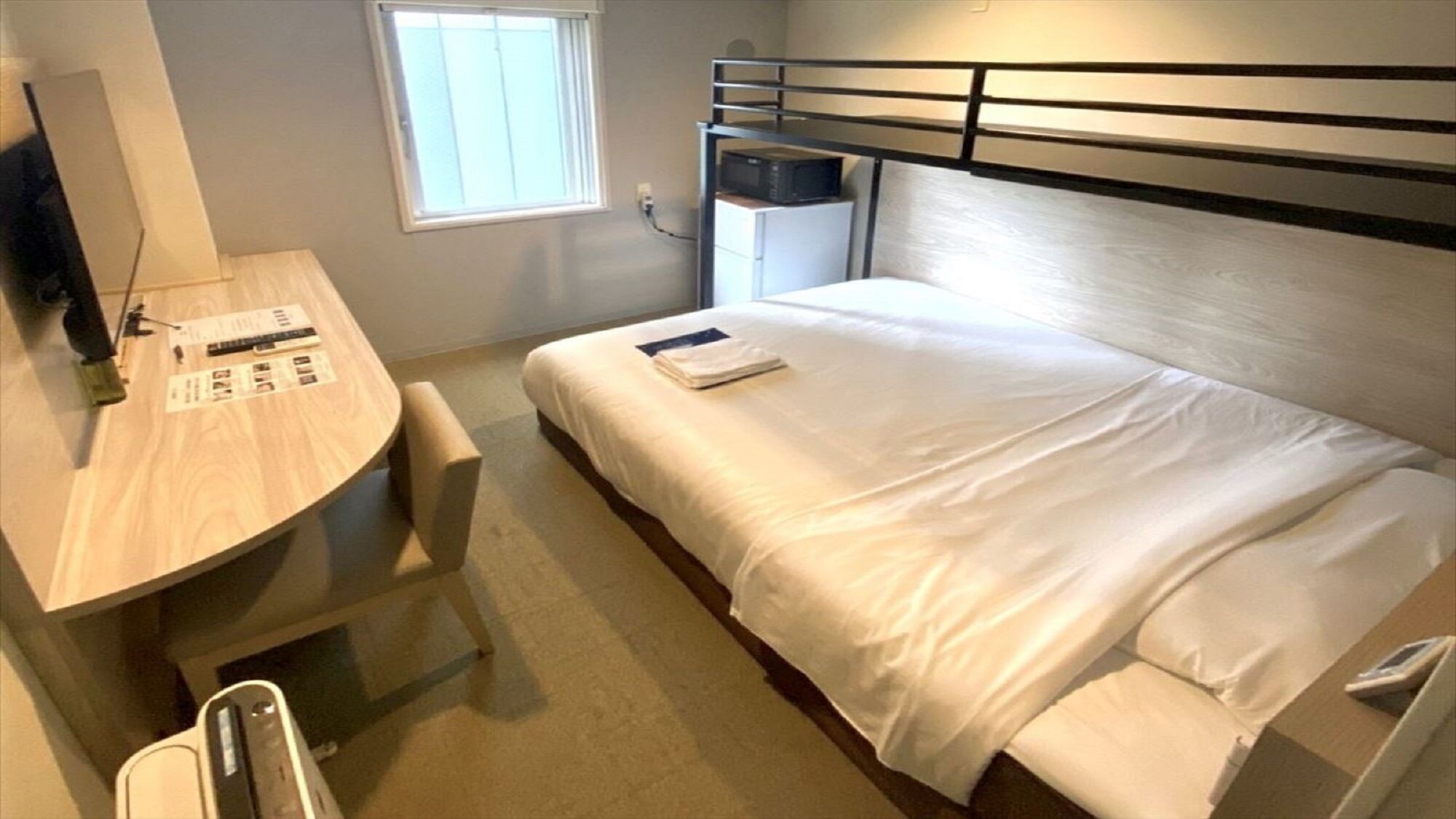 A compact hotel room with a bunk bed, a desk with a chair, a small window, and a microwave.
