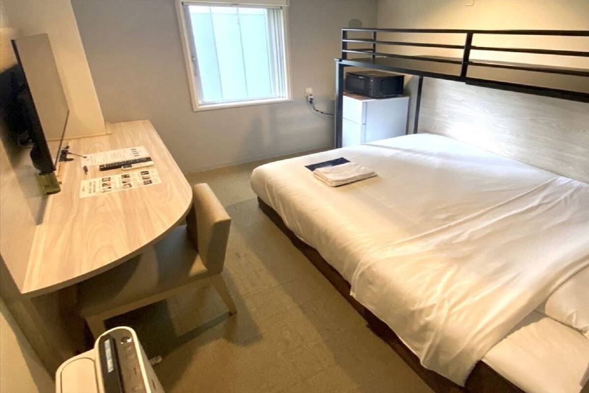 Una camera d'albergo compatta con un letto a castello, una scrivania con sedia, una piccola finestra e un forno a microonde.
