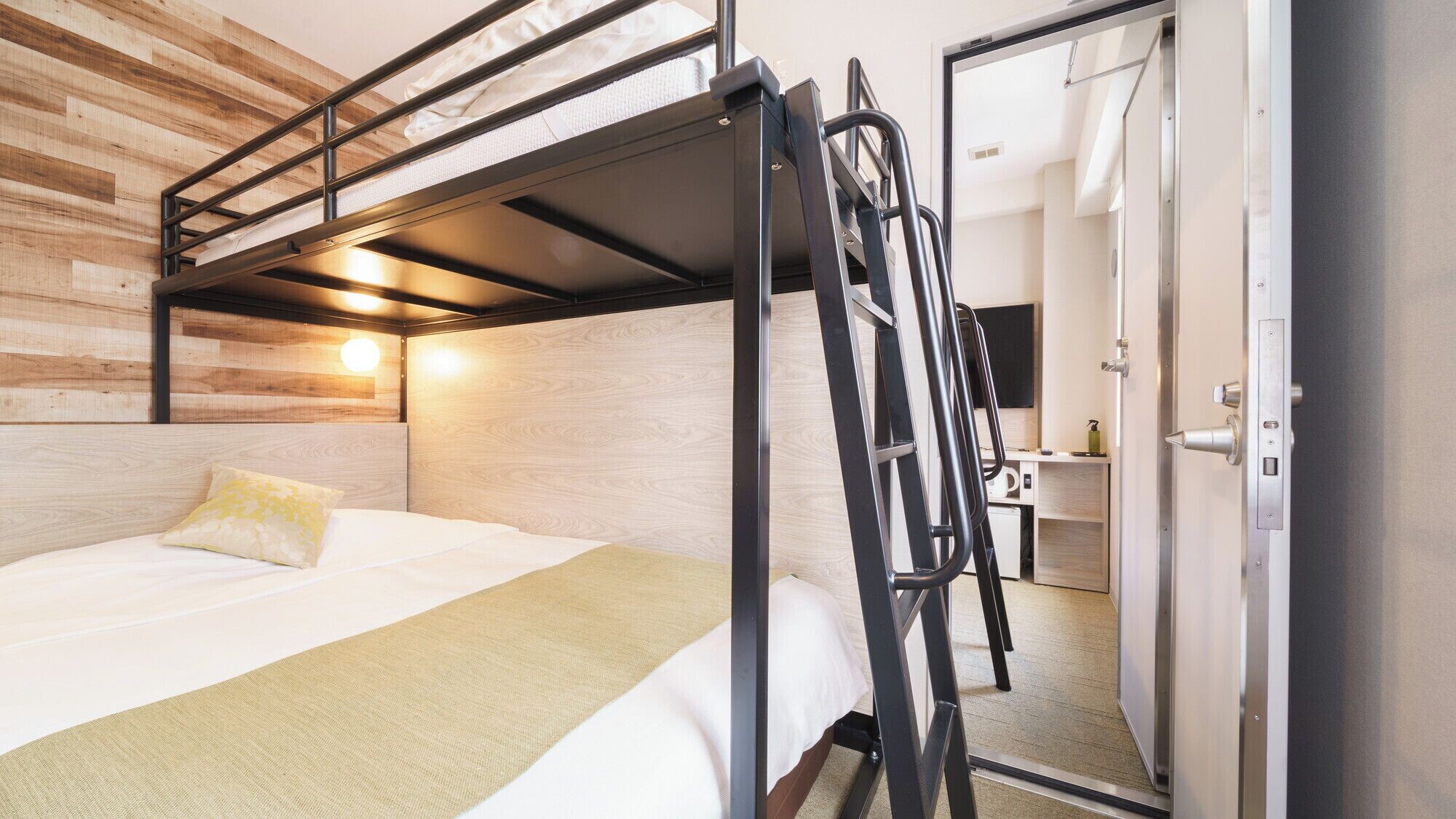 A bunk bed with a ladder, a bedside table, a mirror, and a wooden wall.