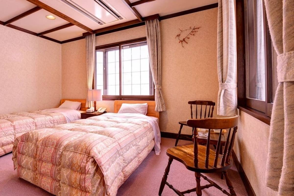 Ein Hotelzimmer mit zwei Betten, einem Holzbett, einem Nachttisch und einem Fenster mit Vorhängen.