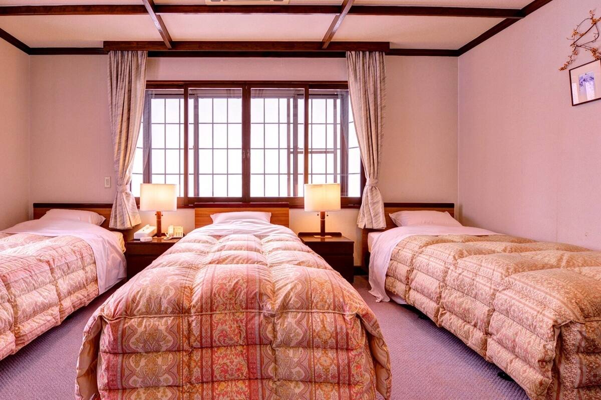 Ein Hotelzimmer mit zwei Betten, einem großen Fenster mit Vorhängen und einer Holzbalkendecke.