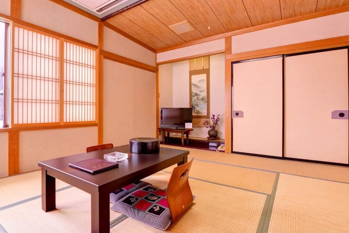 Ein traditioneller japanischer Raum mit Tatami-Böden, einem niedrigen Tisch, einem Fernseher und verschiebbaren Türen.