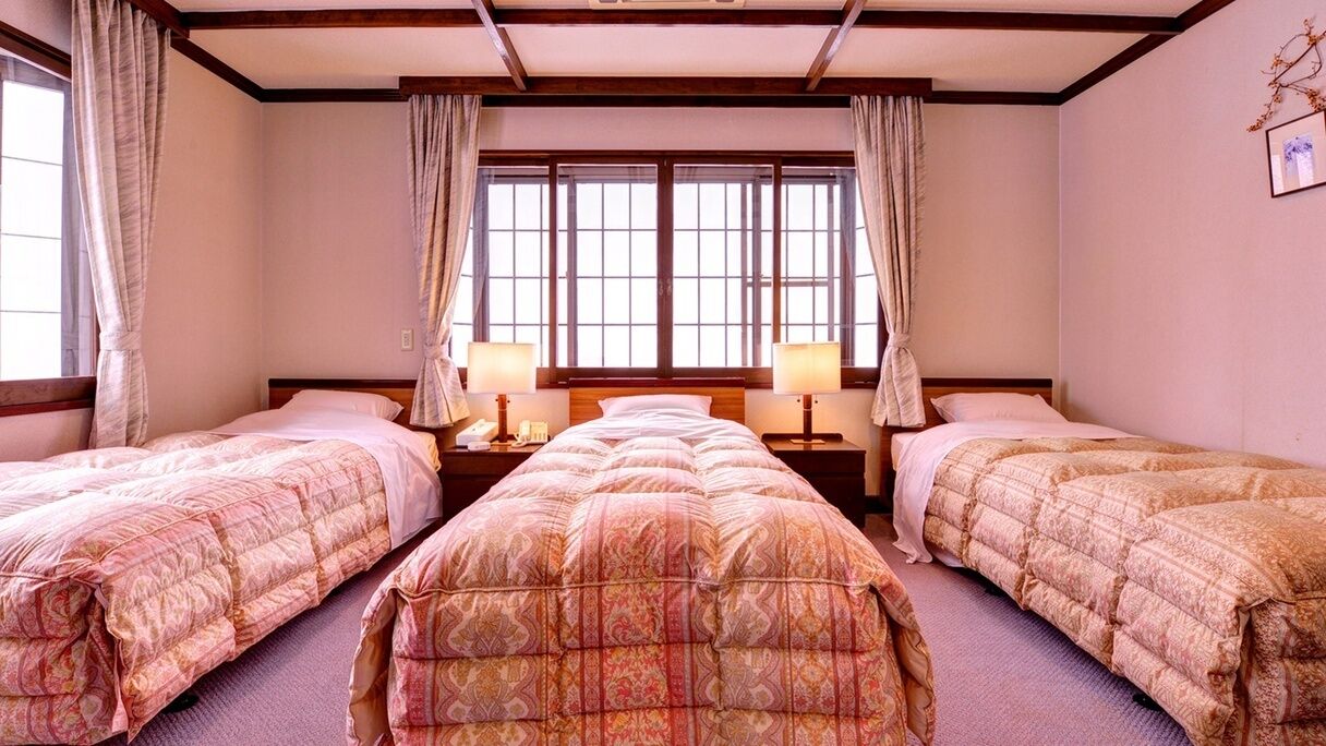 A hotel room with two single beds, a large window with curtains, bedside lamps, and a framed picture on the wall.