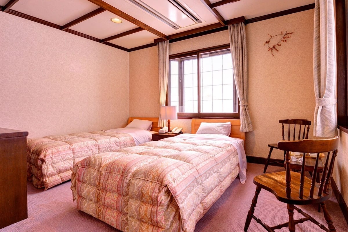 Ein Hotelzimmer mit zwei Betten, einem Sessel, einem Schreibtisch und einem Fenster mit Vorhängen.