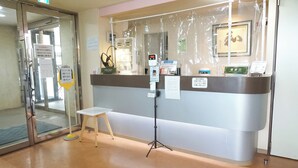 Un espace d’accueil doté d’une porte d’entrée en verre, d’un petit tabouret, d’une horloge numérique et de panneaux d’information.