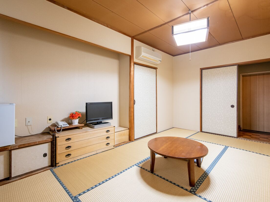 Um quarto japonês tradicional, com tatames, uma mesa de madeira, uma televisão e um pequeno armário.