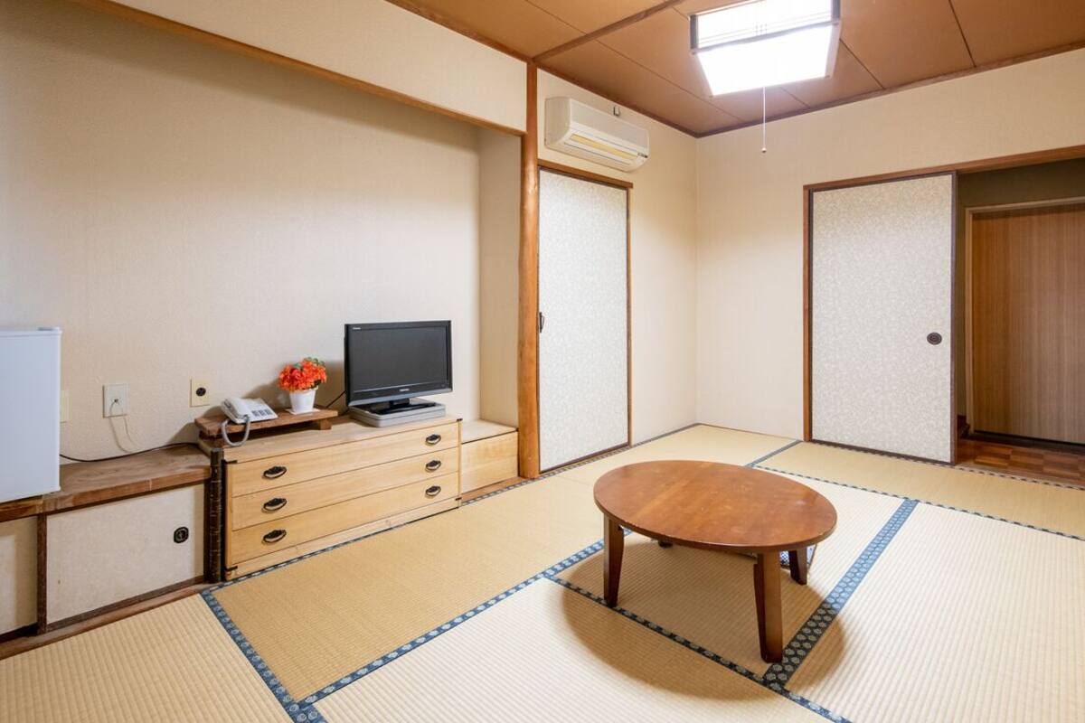 A traditional Japanese room with tatami flooring, a wooden table, a television, and a small cabinet.