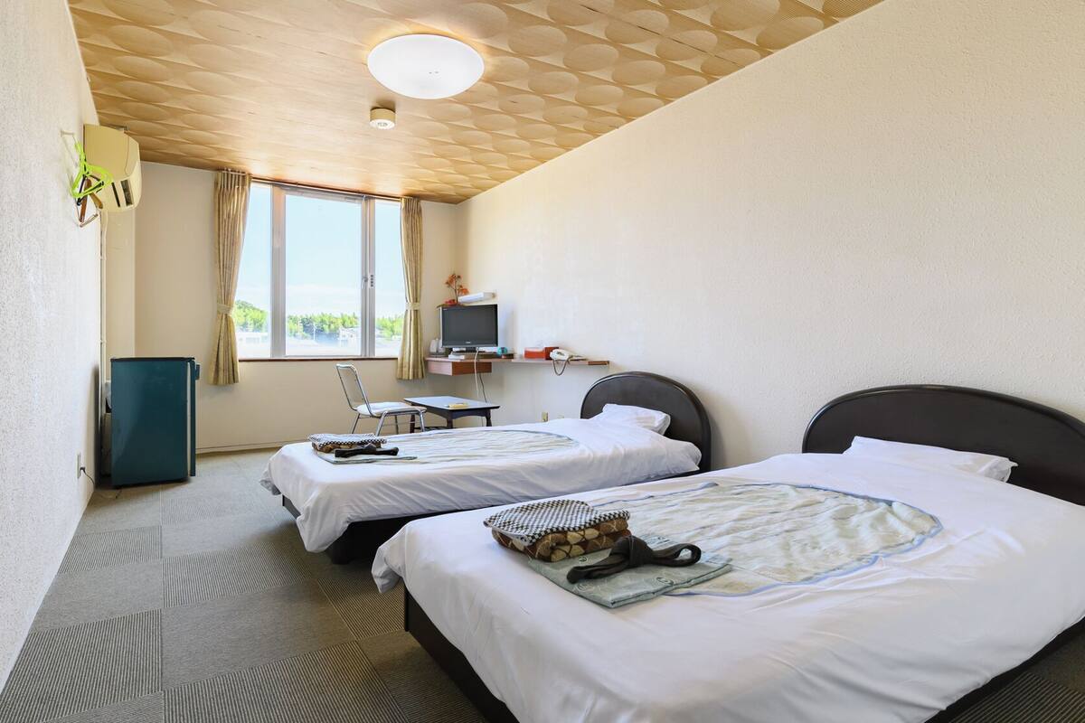 A hotel room with two beds, a desk, a television, and a window with curtains.