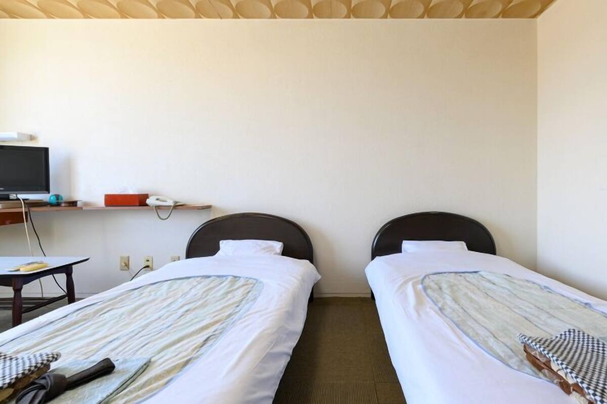 A hotel room with two single beds, a desk with a computer and phone, and a television on a stand.