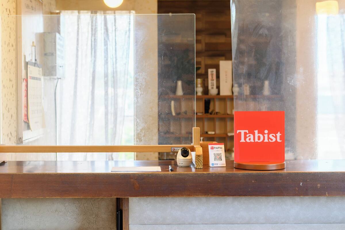 A reception desk with a 'Tabist' sign, a PayPay QR code, and a security camera.