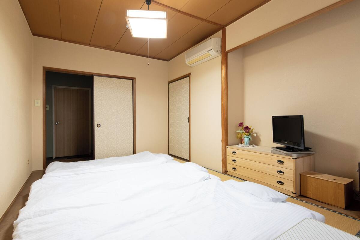 A hotel room with a bed, a dresser, a television, and an air conditioning unit.