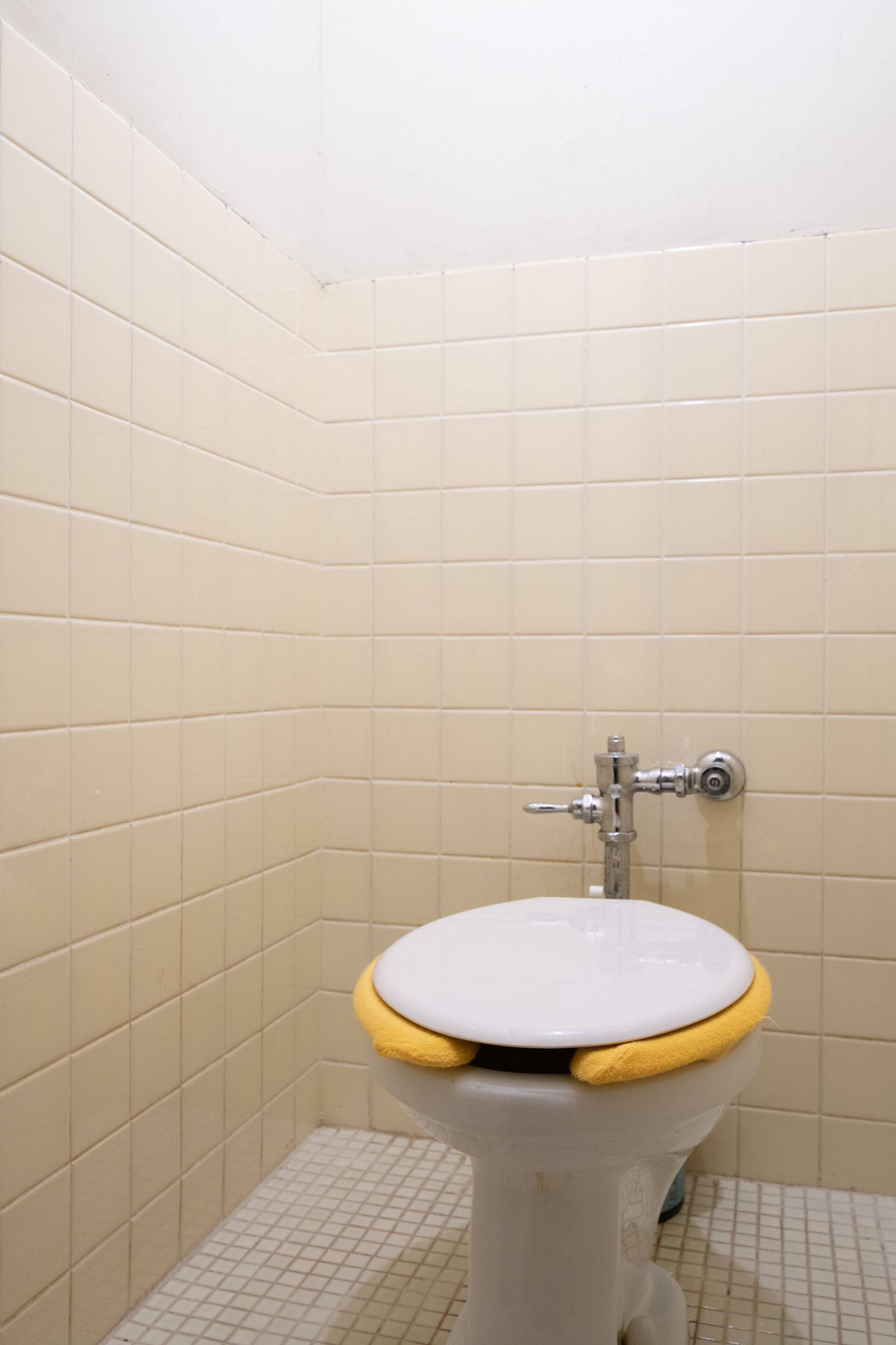 Un inodoro con cubierta amarilla en un baño con paredes de azulejos color beige.