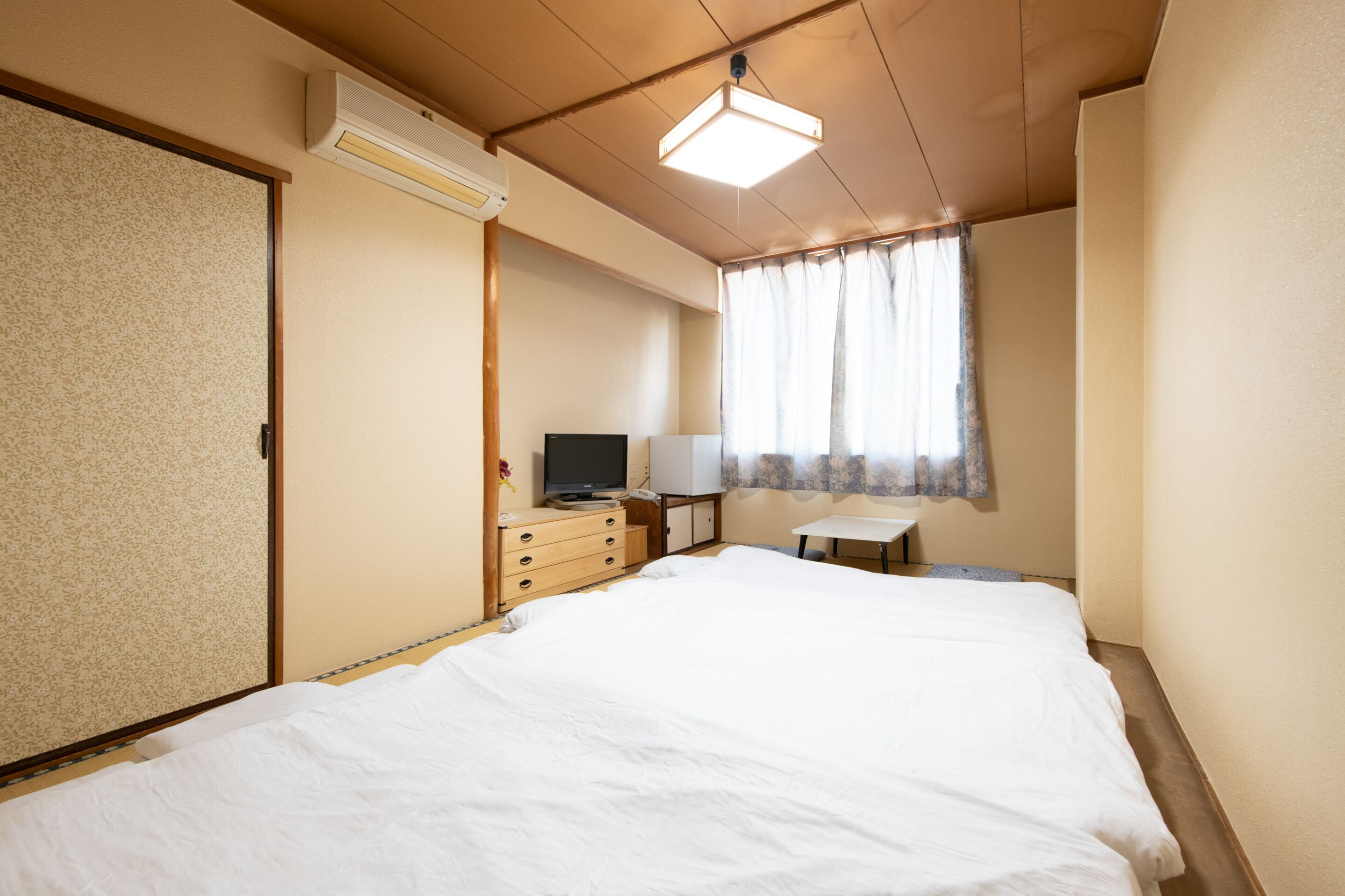 Ein Hotelzimmer mit einem großen Bett, einem Schreibtisch mit Stuhl, einem Fernseher und einem Fenster mit Vorhängen.
