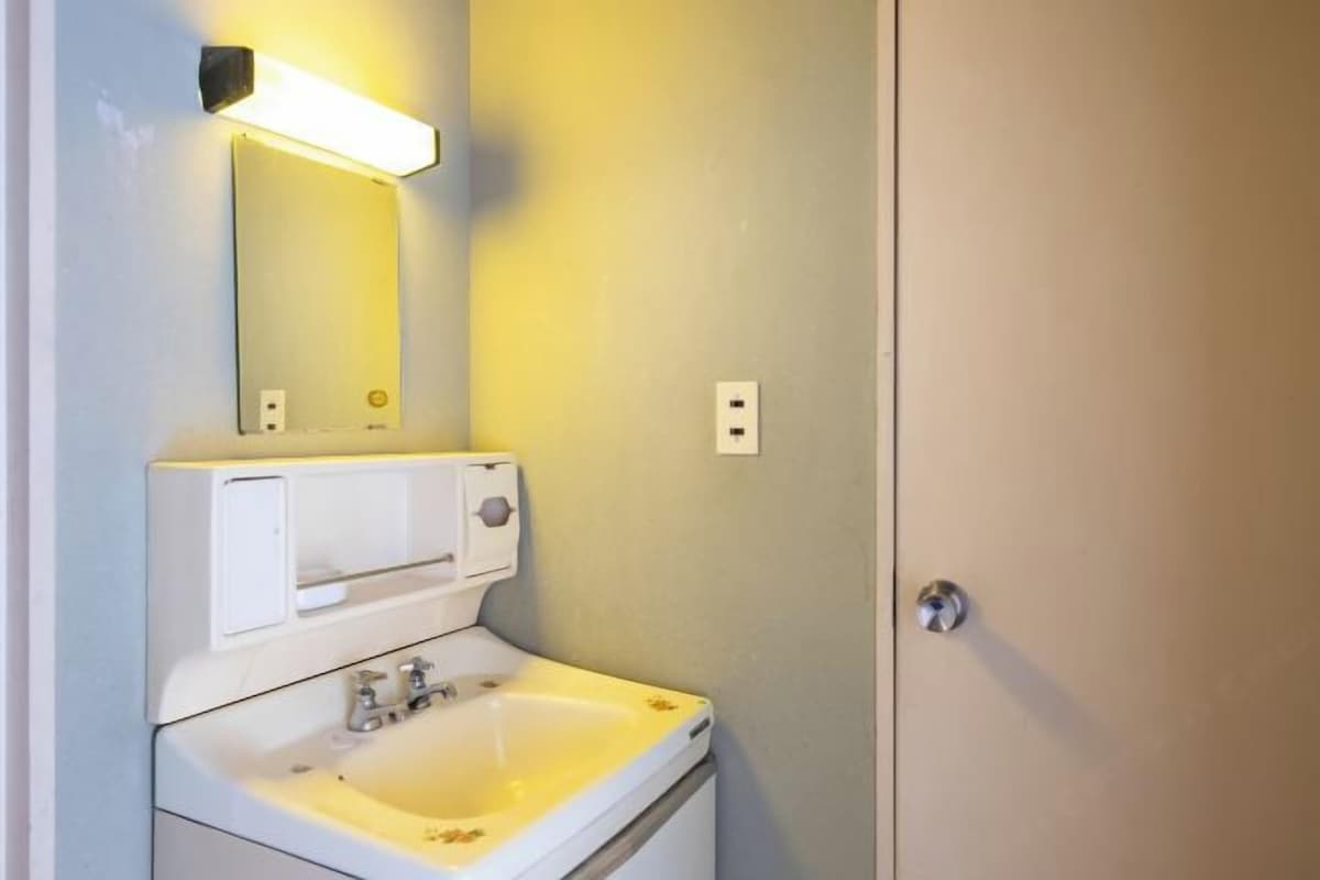 A bathroom with a white sink, a mirror, and a wall-mounted light fixture.