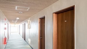 A long, narrow hallway with wooden doors and a fire extinguisher on the left. - Tabist Chunichi Business Hotel Iseshima (Shima)