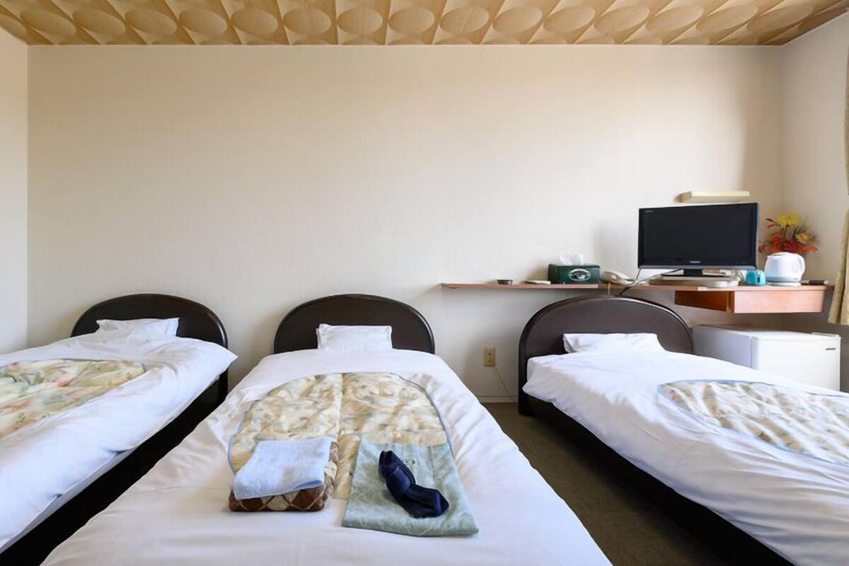 A hotel room with three single beds, a desk with a computer, and a small refrigerator.