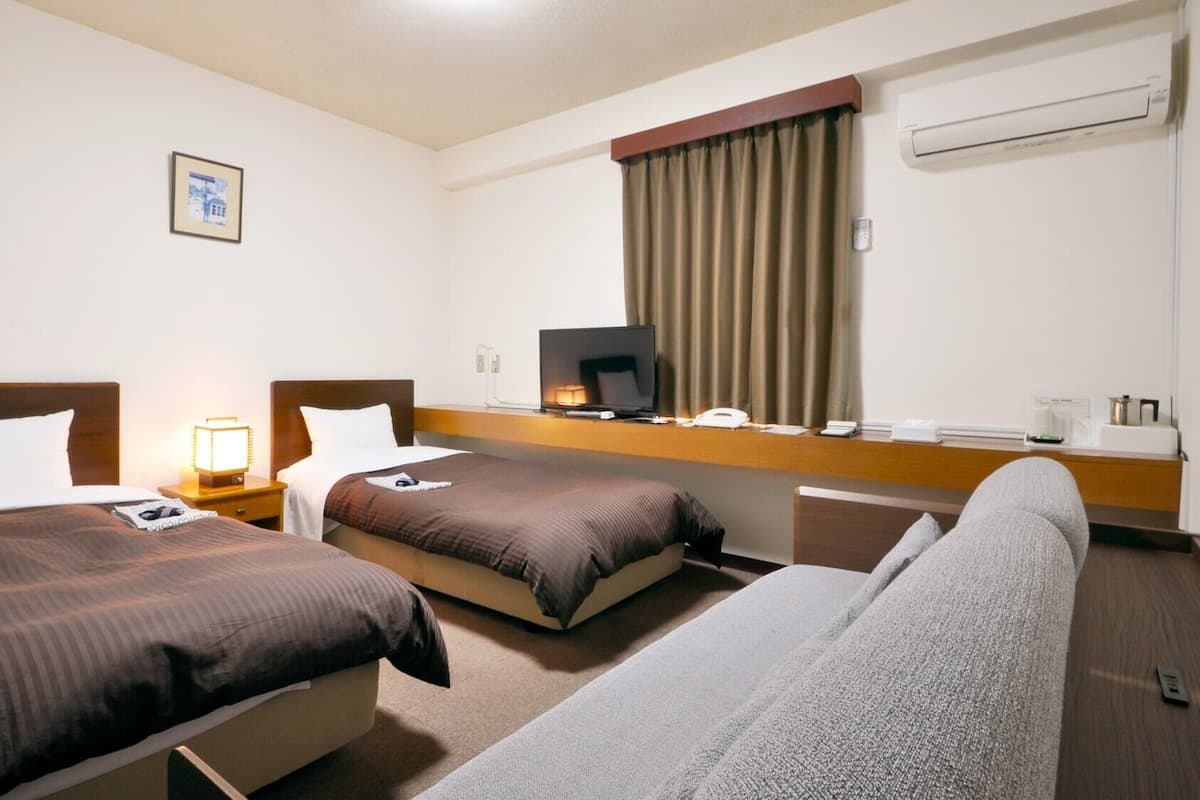 A hotel room with two beds, a desk, a television, and an air conditioning unit.