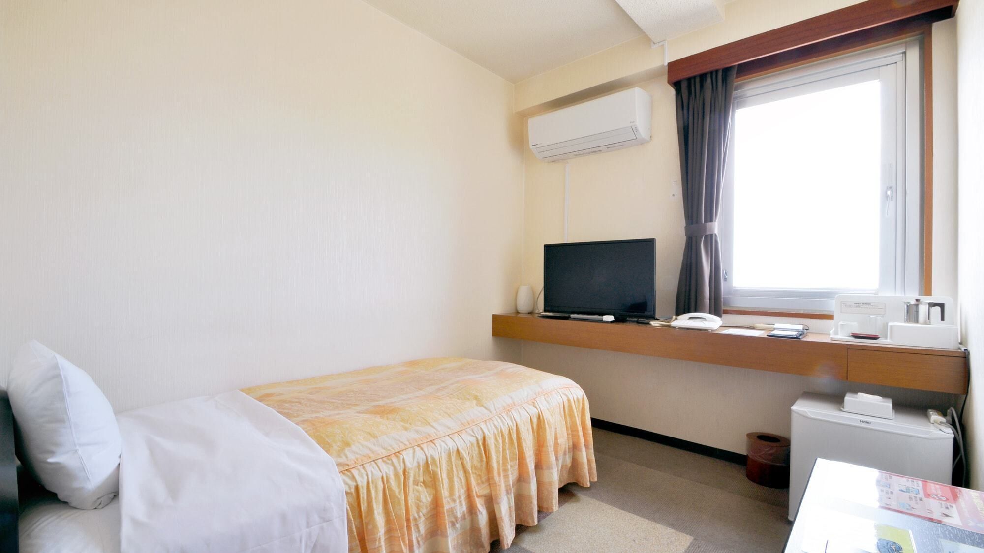 A hotel room with a bed, a desk with a computer, a telephone, and an air conditioning unit.