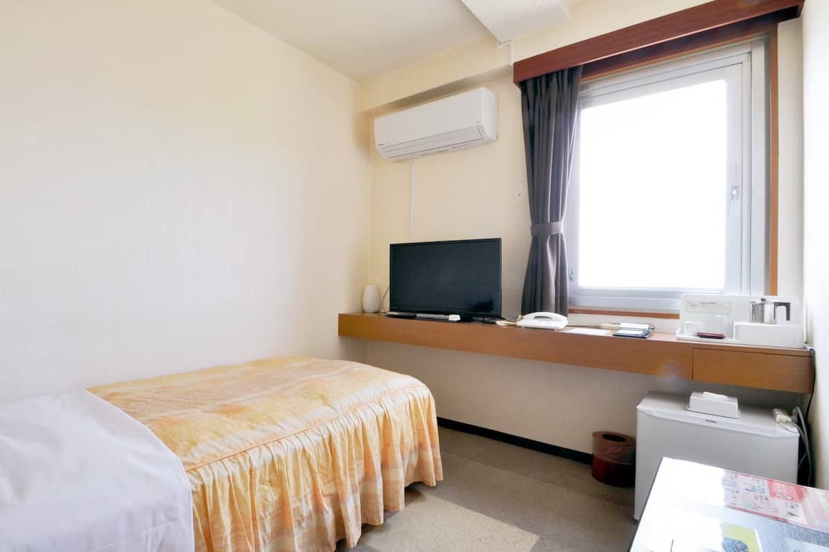 A hotel room with a bed, a desk with a computer, a telephone, and an air conditioning unit.