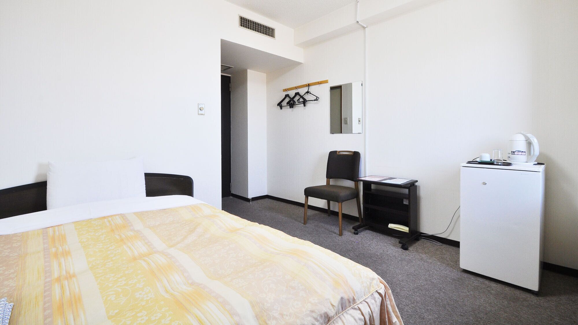 Ein Hotelzimmer mit Bett, Schreibtisch, Stuhl, Kleiderschrank und Spiegel.