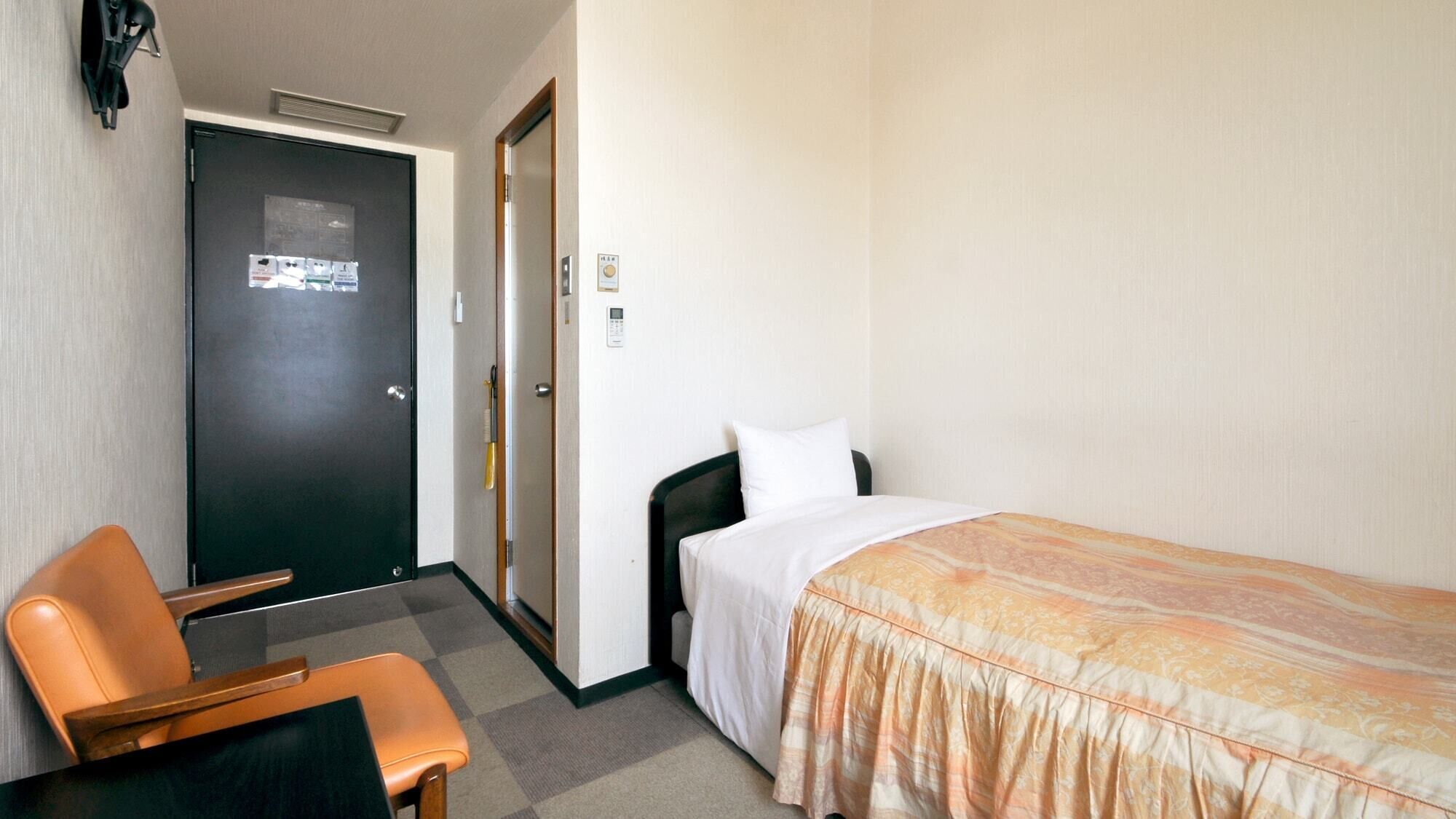 Ein Hotelzimmer mit einem Bett, einem Sessel, einem Schreibtisch, einer Tür und einem an der Wand befestigten Telefon.