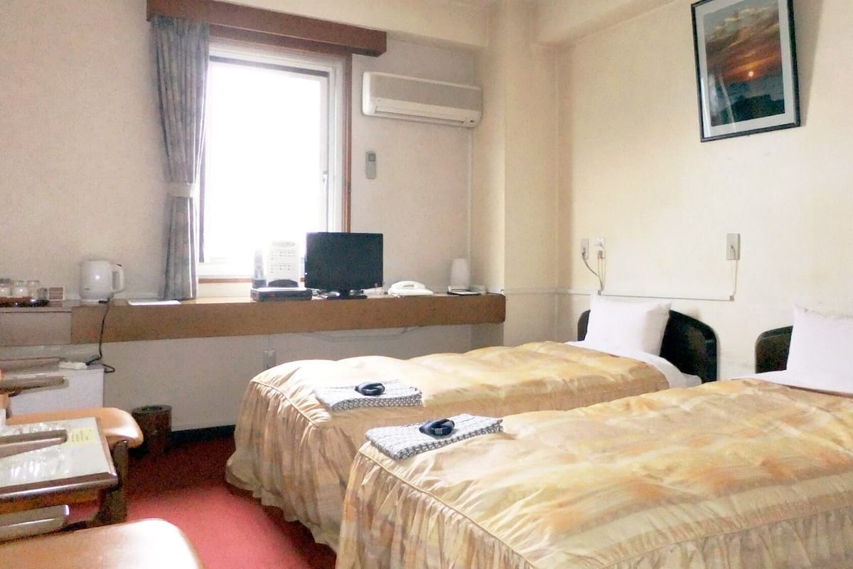 A hotel room with two beds, a desk with a computer, a window with curtains, and a painting on the wall.