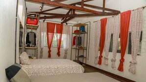 A bedroom with a bed, a wardrobe, a shelf with clothes, and a window with curtains. - YAKU eco house (La Banda de Shilcayo)