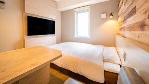 A bedroom with a bed, a wooden desk, a TV mounted on the wall, and a window.