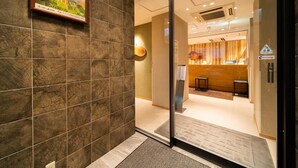 A hotel lobby with a reception desk, a wall-mounted poster, and a tiled floor.