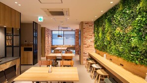 A modern restaurant interior with wooden tables and chairs, a brick wall, and a green vertical garden.