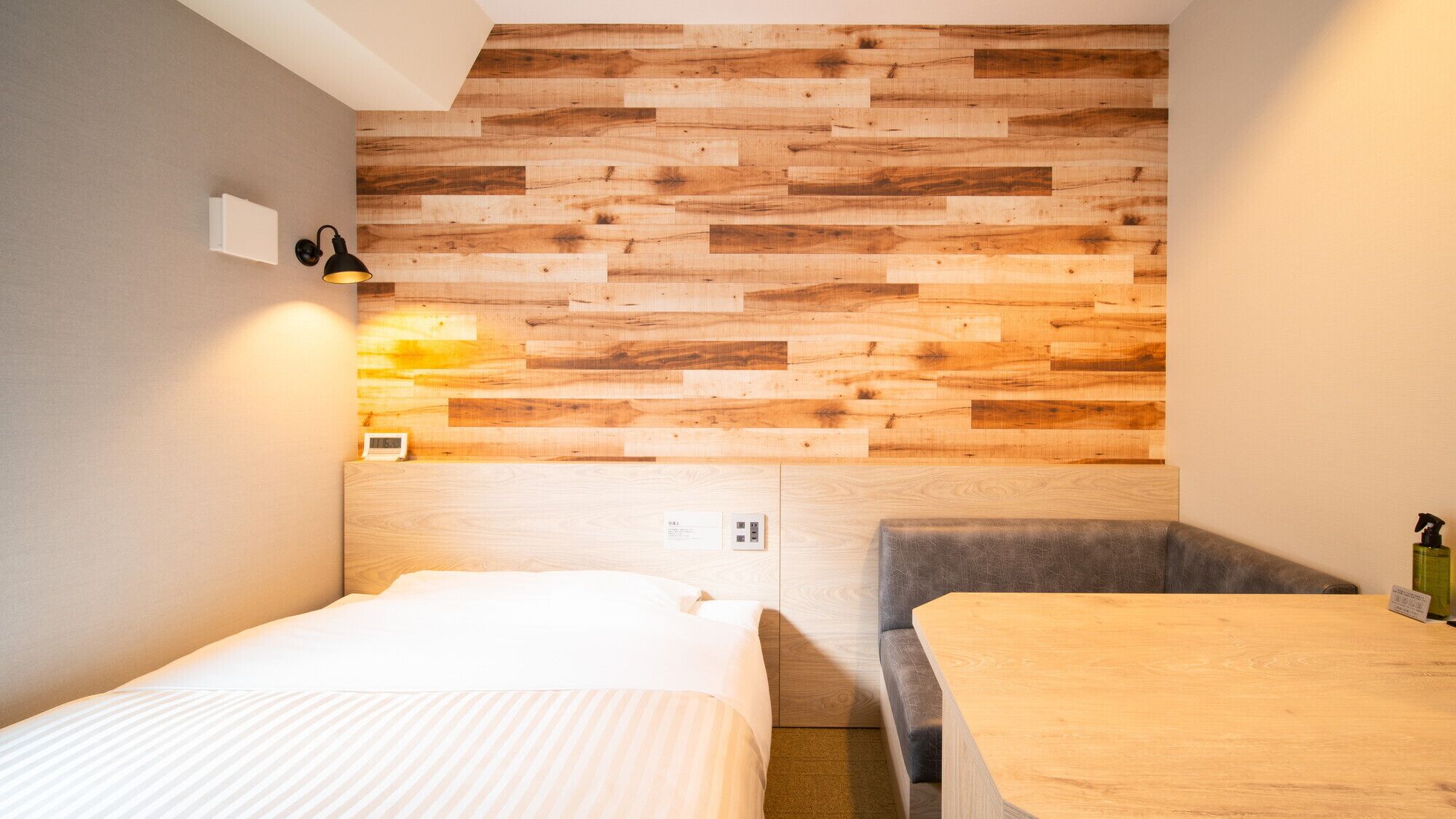 A small, modern room with a wooden wall panel, a bed, a chair, and a table.