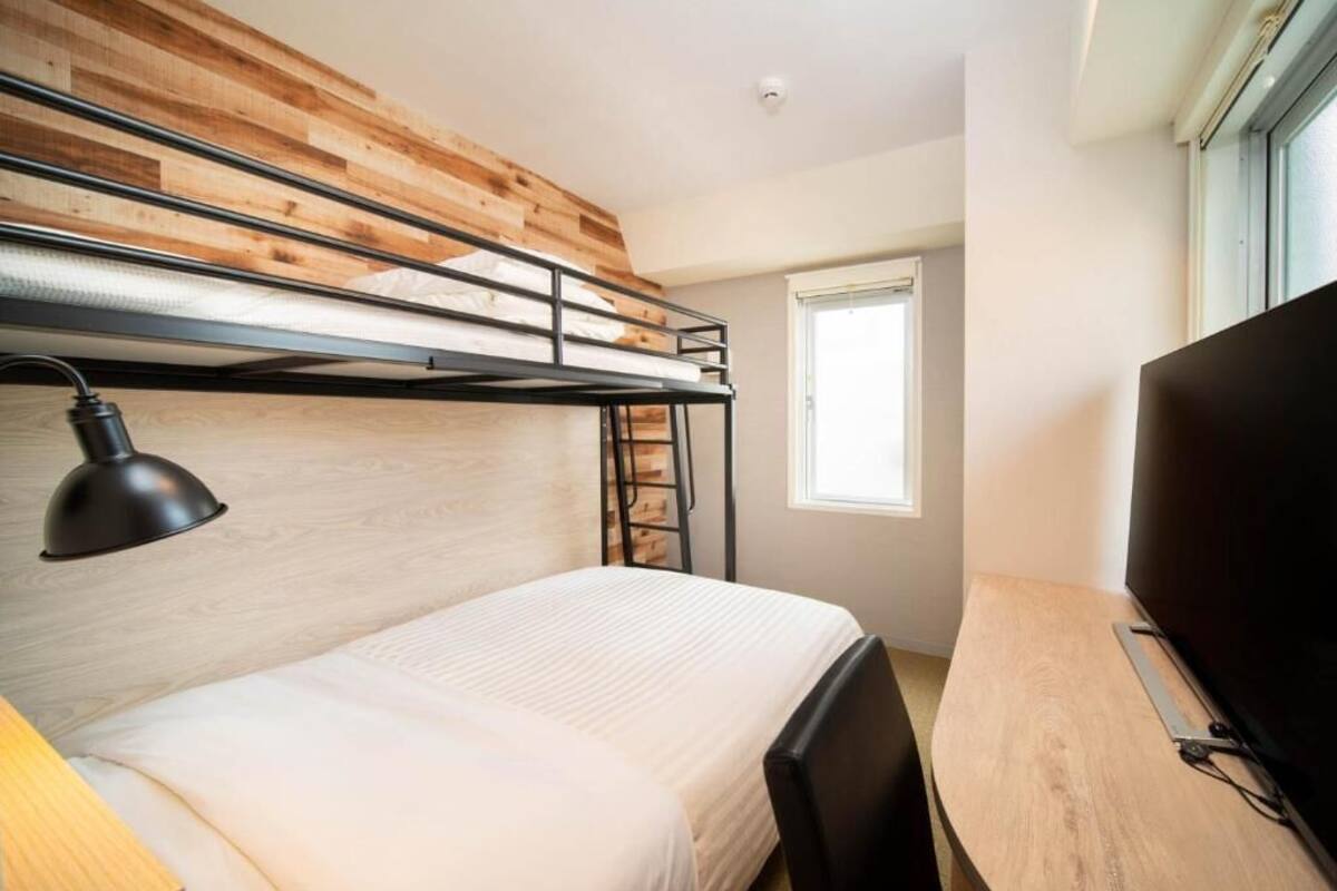 Een stapelbed met een bureau en een televisie in een kamer met houten lambrisering en een raam.