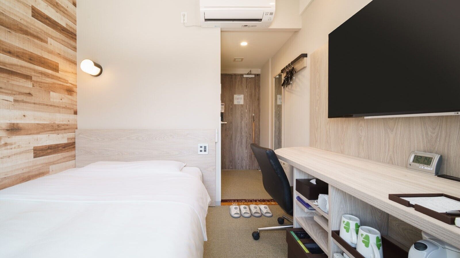 A hotel room with a bed, a desk with a flat-screen TV, a chair, and a small bathroom.